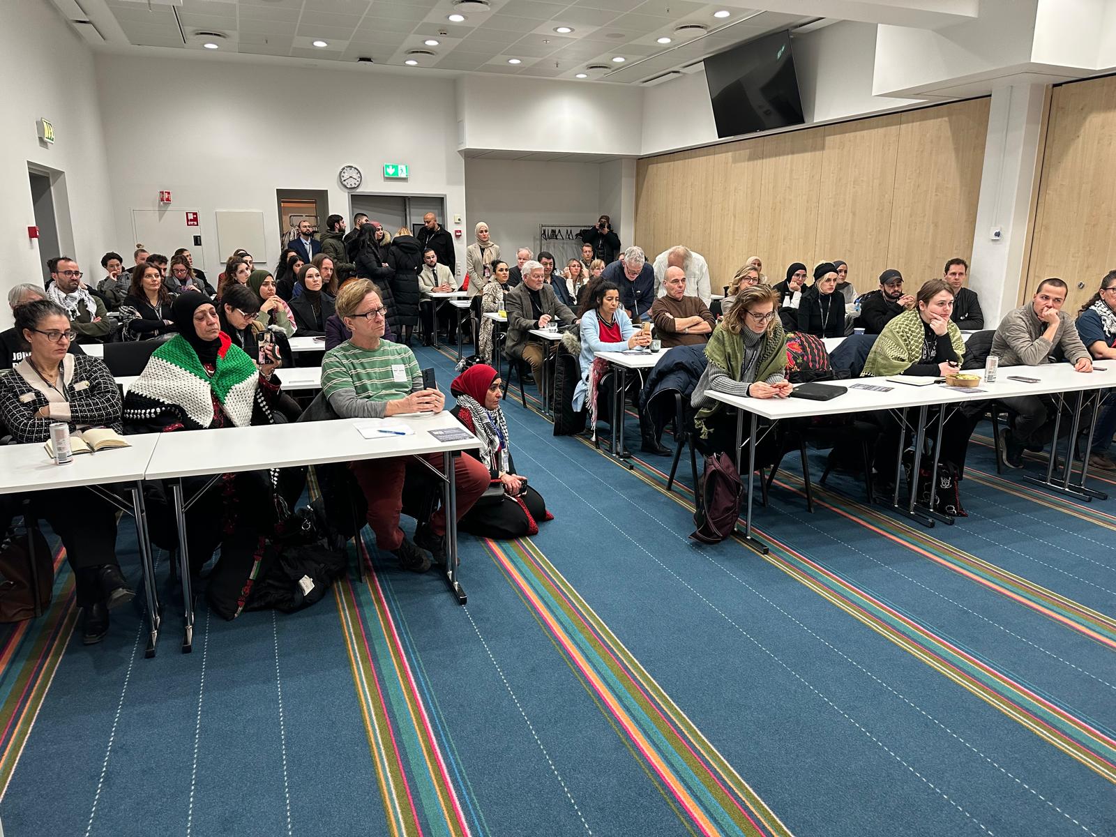 Workshop room with participants at long tables and small Palestinian flags on the tables.