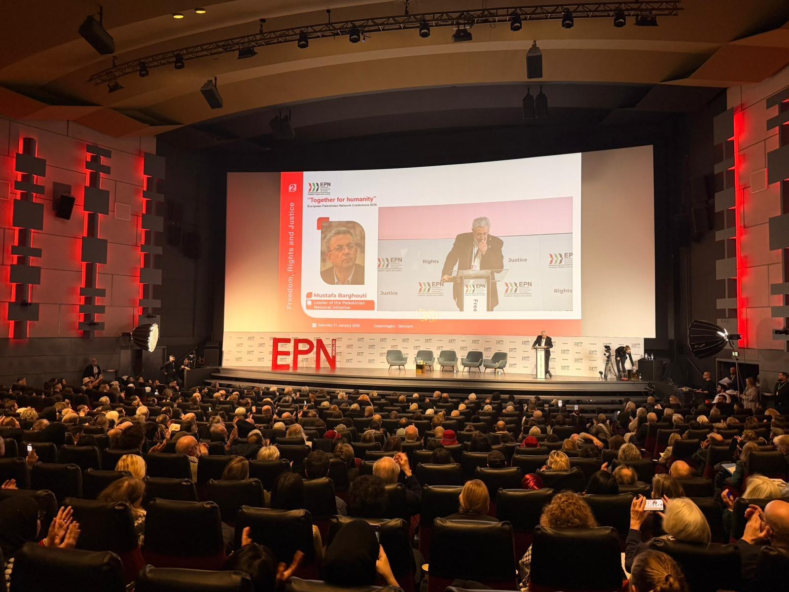 Speaker at the lectern; the screen shows the speaker portrait and the EPN letters stand in front of the stage.